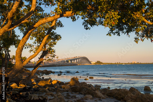 Fort Myers Bridge, Florida, view through the wooden branches tree from the beach on warm afternoon golden sun light, The Sanibel Island Causeway photo
