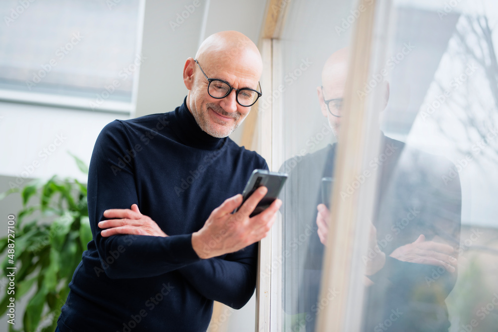 Smiling man holding a cellphone in his hand and text messaging Smiling man holding a cellphone in his hand and text messaging