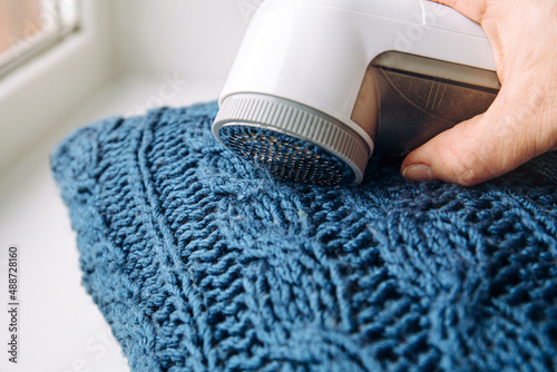 Removing shaving lint fuzz from blue woolen coat sweater, wool clothes maintain concept. photo