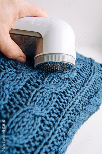 Removing shaving lint fuzz from blue woolen coat sweater, wool clothes maintain concept.