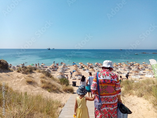 grandmother and granddaughter walking from above towards the beach. people on the beach holiday background