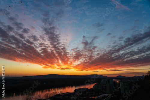 Dramatic sunset clouds over black silhouetted hills with red reflection in river, wide-angle panorama 