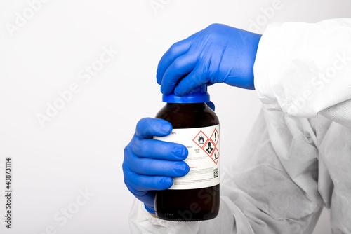 Scientist holding nitric acid in laboratory environment. It shows the way of use before the experiment. He has blue gloves on his hands