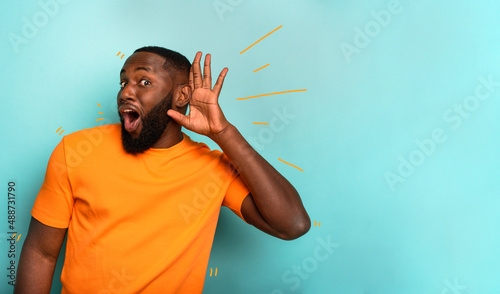 Man speaks in the ear to a friend about a great promotion. amazed expression. cyan background photo