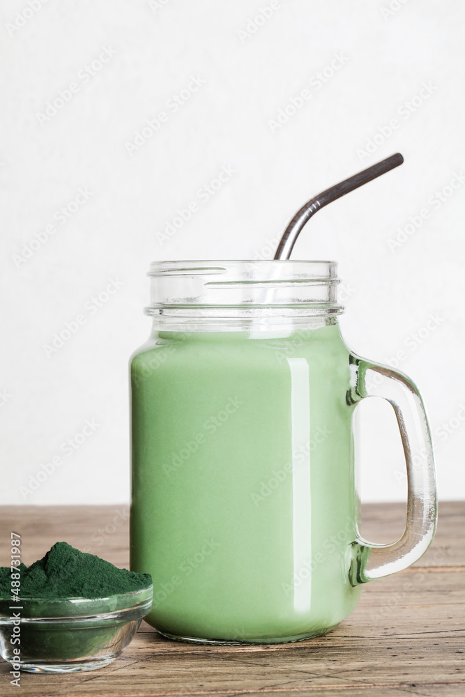 fresh green smoothie in glass bottle and spirulina powder with spoon on wooden background. useful habits, self care and healthy lifestyle. copy space fresh green smoothie in glass bottle and spirulina powder with spoon on wooden background. useful habits, self care and healthy lifestyle. copy space