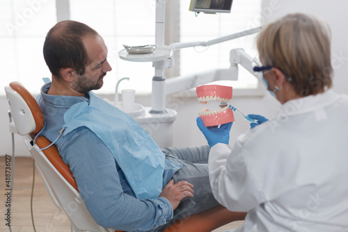 Dpecialist orthodontist showing ceramic jaw model to patient with toothache discussing carier treatment during stomatology consultation in dentistry office room. Doctor woman explaining oral hygiene photo