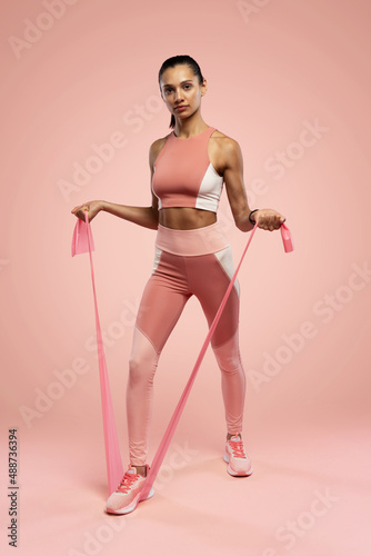 Sportswoman exercising with resistance band. Female with working out with elastic band on pink background © opolja