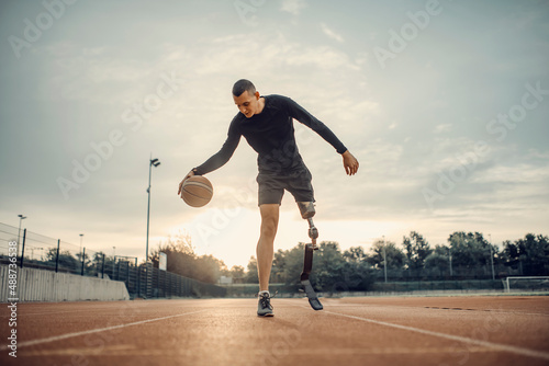 Fototapeta A handicapped sportsman with prosthetic leg dribble the basketball at stadium