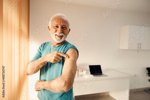 Bild auf Leinwand A happy senior man in doctor's office pointing at his vaccinated shoulder