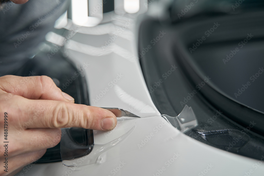 Skilled worker removing excess PPF on auto body panel