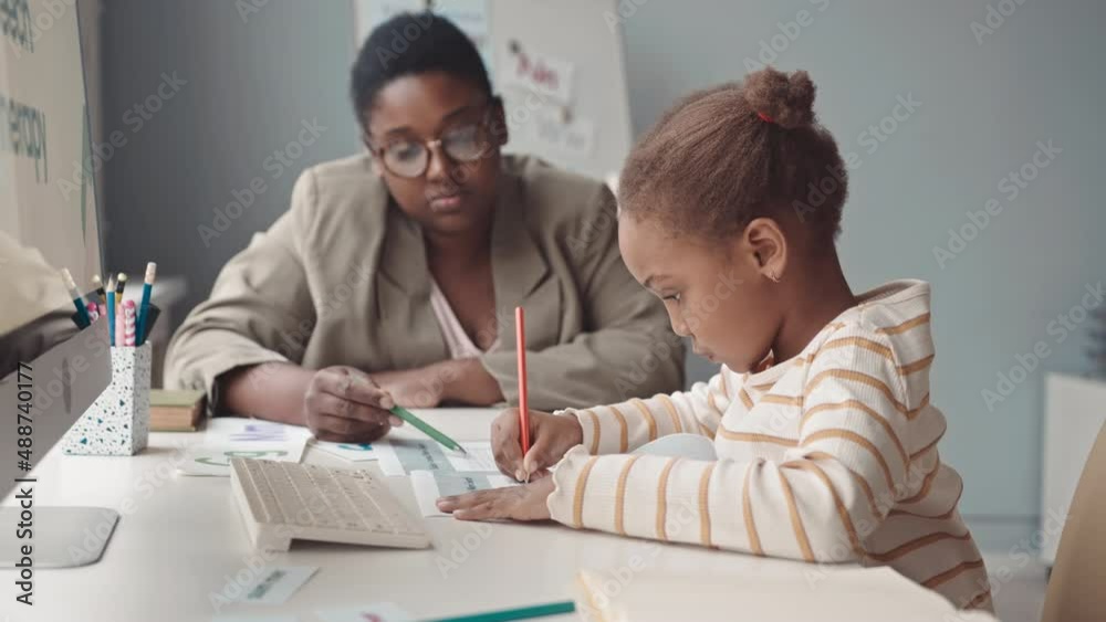 Waist up slowmo of 5 year old African-American girl and female teacher having speech therapy lesson in modern white classroom