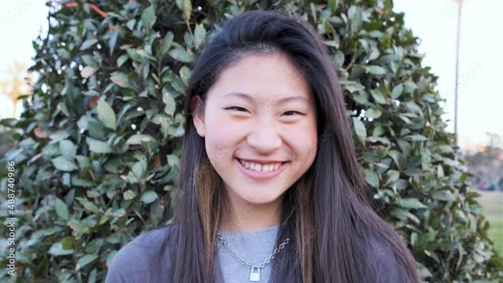 Young Asian woman looking at the camera and smiling while standing outdoors on the street. Young Asian woman looking at the camera and smiling while standing outdoors on the street.