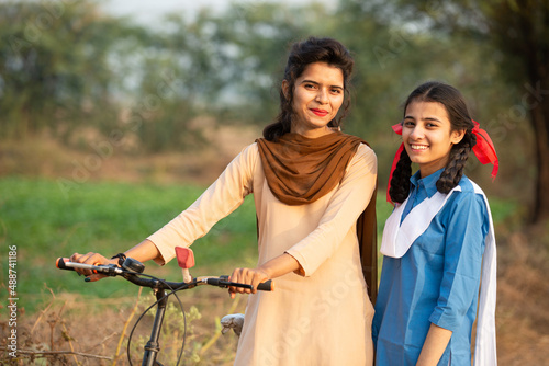 Portrait of happy young rural indian girls wearing school uniform standing with bicycle at village street. Two Female friends smiling.