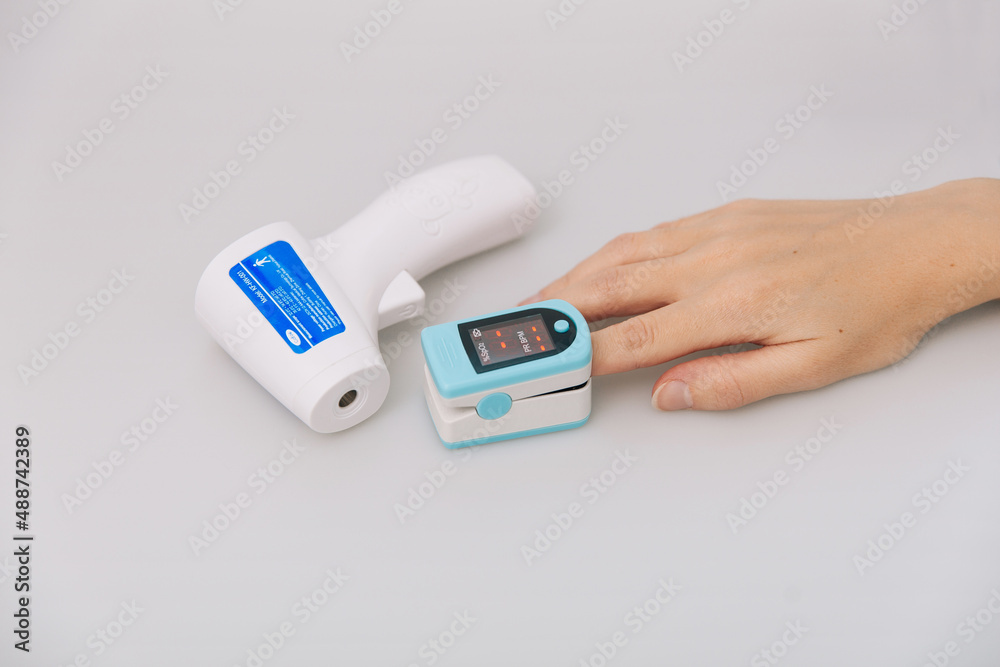 Pulse oximeter and thermometer gun on white background. Infrared isometric thermometer gun to check body temperature for virus symptoms. Measuring oxygen saturation, pulse rate and oxygen levels. Pulse oximeter and thermometer gun on white background. Infrared isometric thermometer gun to check body temperature for virus symptoms. Measuring oxygen saturation, pulse rate and oxygen levels.
