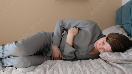 Stressed young woman lying on bed, embracing belly, suffering from stomachache or menstrual painful feelings. Gastritis, abdominal or period pain concept. photo