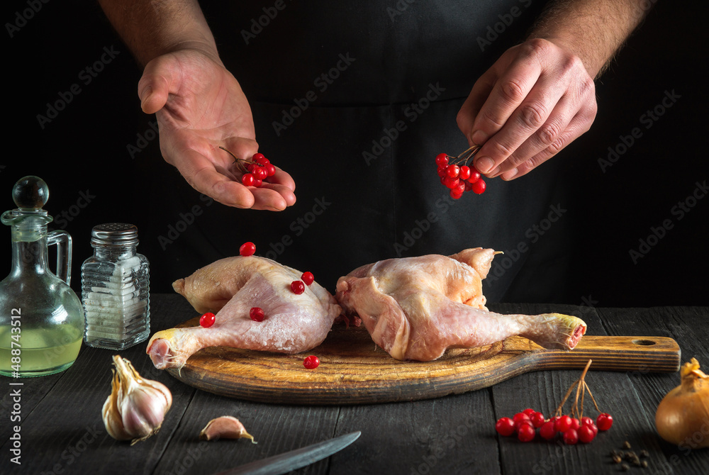 Chef prepares raw chicken legs in the restaurant kitchen. The cook puts the red viburnum on the chicken leg before baking. Asian cuisine