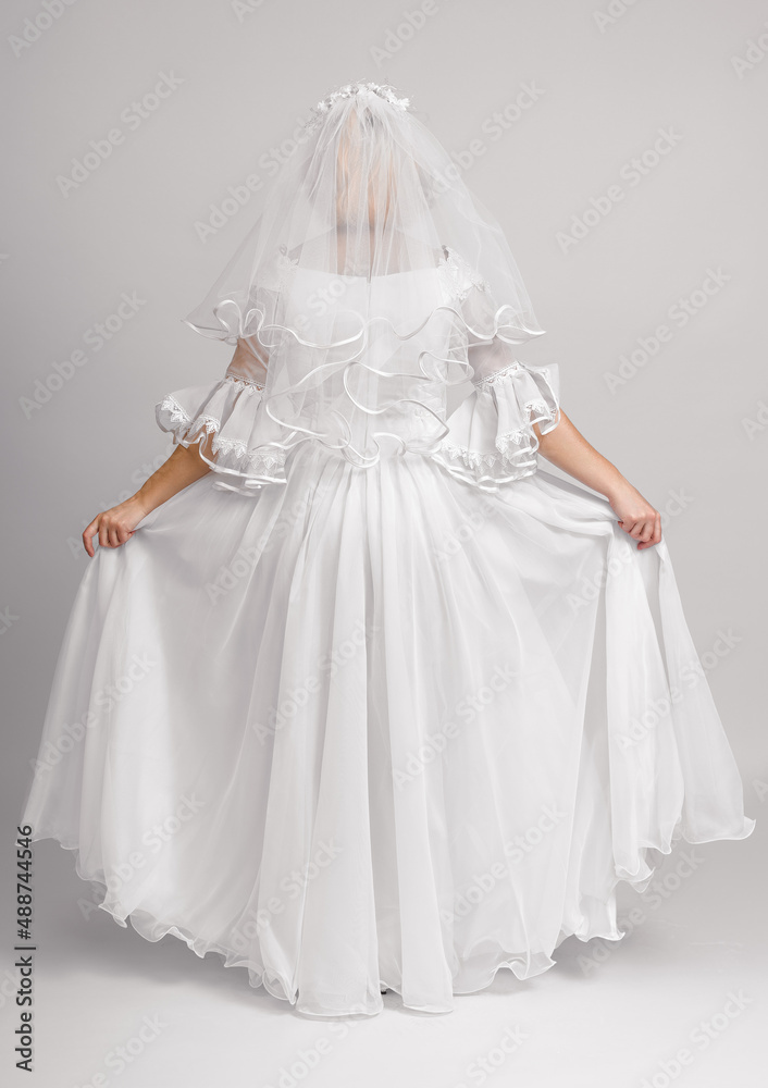 the bride stands with her back in a veil and demonstrates a wedding dress on a white background in full growth the bride stands with her back in a veil and demonstrates a wedding dress on a white background in full growth