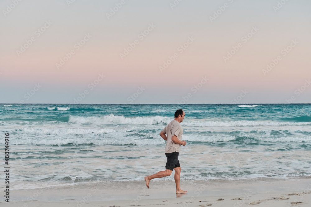 Senior asian man running barefoot on sandy ocean beach at sunrise. Senior asian man running barefoot on sandy ocean beach at sunrise.