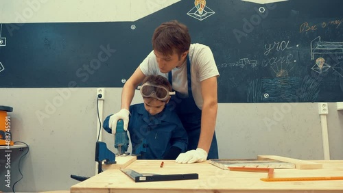 By cutting the wood. Child and teacher build a piece of furniture together during an extra curricular activity at school photo