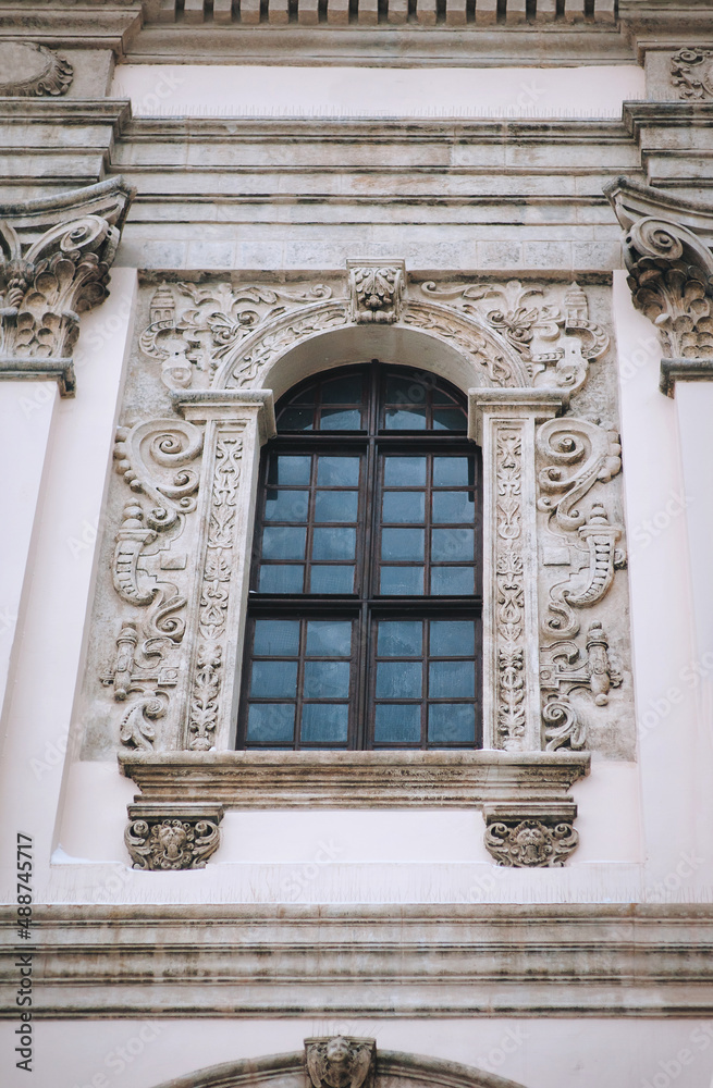 Antique baroque window with a wooden brown frame, decorated with decorative stucco on a gray wall. Jesuit Church in Lvov.