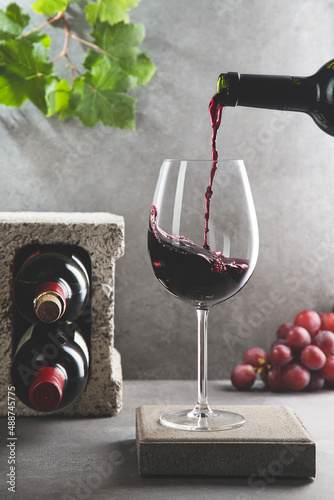 Bottle of red wine poured into the wine glass on concrete background. Vertical format. Beverage and wine concept.