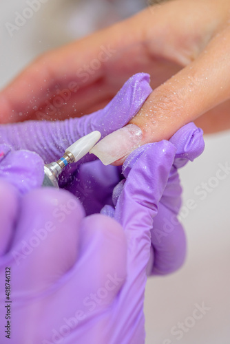 Closeup shot of woman in nail salon receiving manicure by beautician with nail file and machine. Woman getting nail manicure.