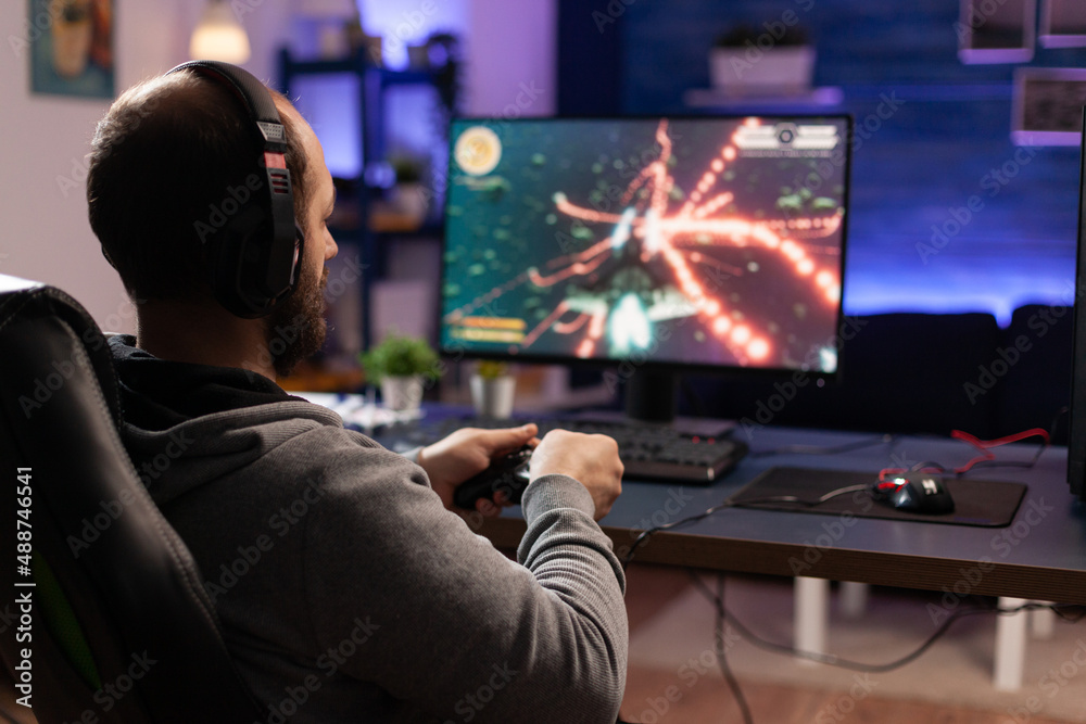 Person playing video games with controller on computer. Player using  joystick and wearing headphones to play online game on monitor. Modern man  using gaming equipment to have fun. Stock Photo