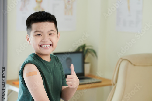 Portrait of happy Asian boy smiling at camera and showing the thumb up after vaccination at hospital