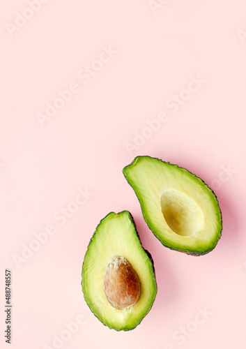 Flat lay of one halved fresh avocado over minimal pink background. Raw natural food.