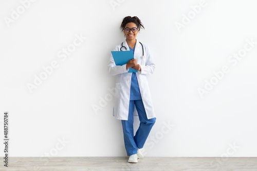 Portrait of black doctor posing with clipboard at white studio