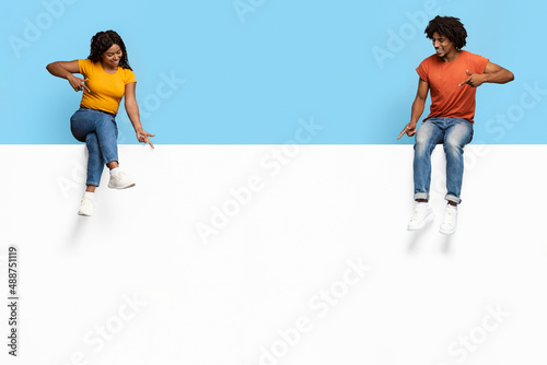 Stylish black people sitting on empty advertising board