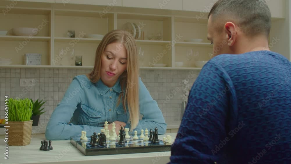 Charming concentrated woman making move with chess piece and checkmate male opponent, celebrating victory with friendly handshake while couple playing chess game at home.