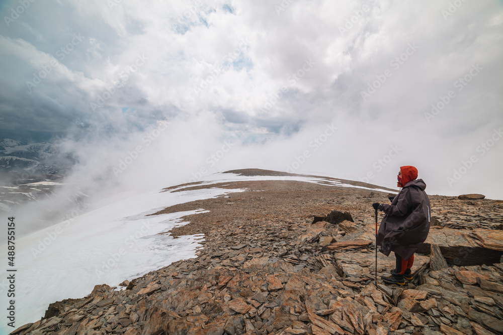 Awesome minimalist mountain landscape with hiker at very high altitude in dense low clouds. Wonderful alpine scenery with man on stone hill with snow in thick clouds. Man and majestic mountains nature Awesome minimalist mountain landscape with hiker at very high altitude in dense low clouds. Wonderful alpine scenery with man on stone hill with snow in thick clouds. Man and majestic mountains nature