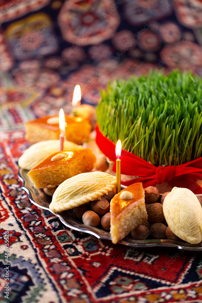 Beautiful Novruz tray on rug with semeni - wheat grass, pakhlava, shekerbura and festive candles on national Azerbaijani carpet table cloth. Spring equinox and new year celebration in Baku. Beautiful Novruz tray on rug with semeni - wheat grass, pakhlava, shekerbura and festive candles on national Azerbaijani carpet table cloth. Spring equinox and new year celebration in Baku.