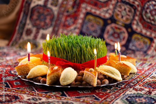Beautiful Novruz tray on rug with semeni - wheat grass, pakhlava, shekerbura and festive candles on national Azerbaijani carpet table cloth. Spring equinox and new year celebration in Baku.
