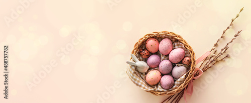 Photo Basket with painted Easter eggs, bunny and willow branches on light background w