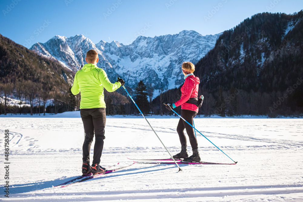 Caucasian couple cross country skiing one behind the other, making coordinated body and ski poles movements.