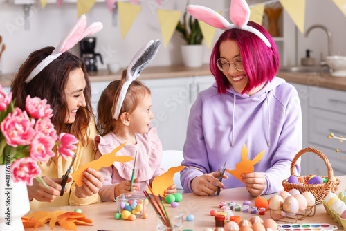 Young lesbian couple with little daughter making Easter decoration in kitchen