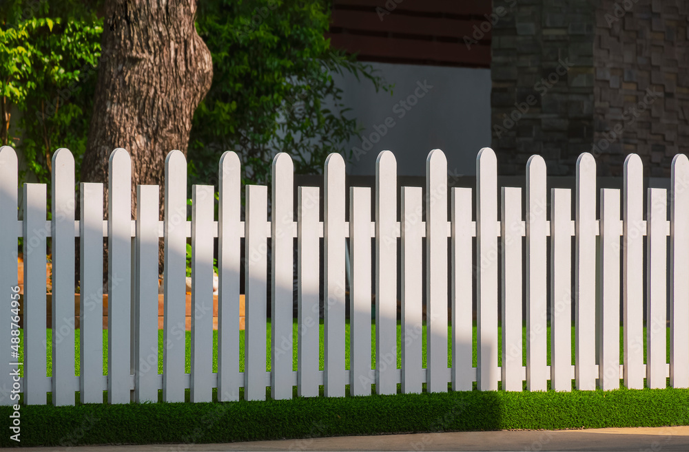 Front view of white wooden fence on artificial turf with sunlight and shadow on surface in front yard area at home Front view of white wooden fence on artificial turf with sunlight and shadow on surface in front yard area at home
