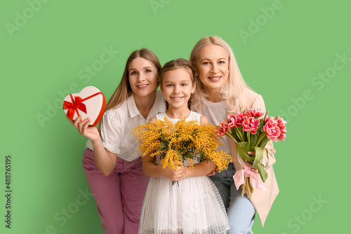 Young woman with her little daughter, mother and gifts on green background. International Women's Day
