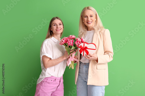 Young woman with her mother and gifts on green background. International Women's Day