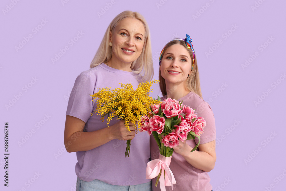 Young woman with her mother and flowers on lilac background