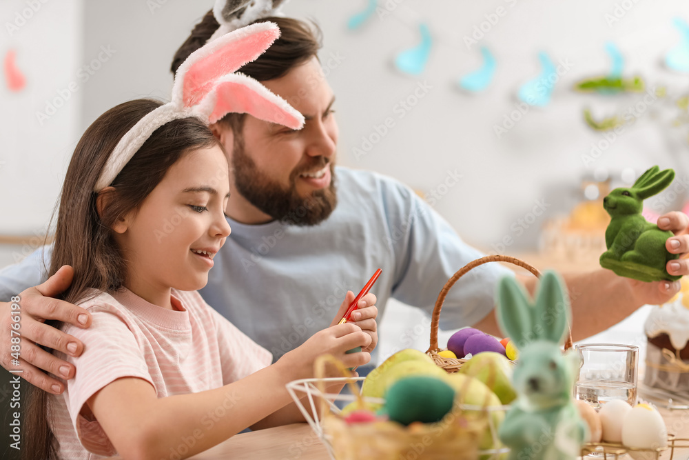 Fototapeta premium Cute little girl with her father painting Easter egg in kitchen