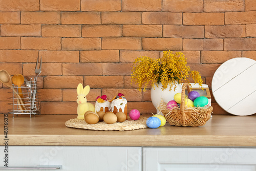 Canvas Print Easter eggs, cakes, rabbit and mimosa flowers on kitchen counter near brick wall
