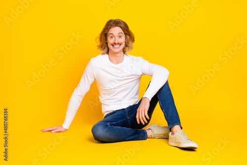 Photo of dreamy excited guy dressed white shirt sitting floor smiling isolated yellow color background © deagreez