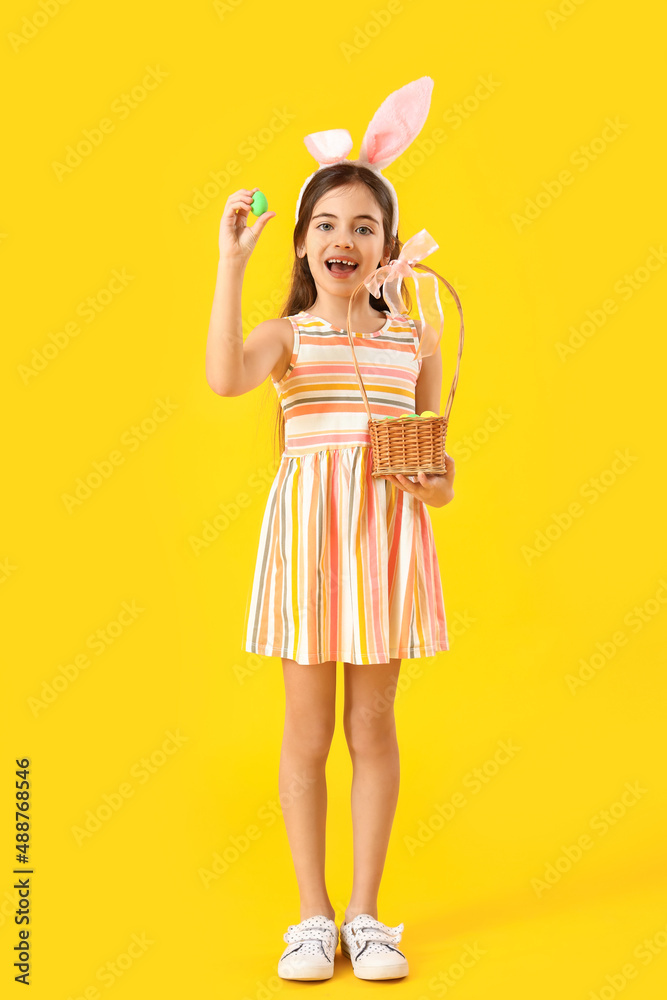 Cute little girl with bunny ears and Easter basket on yellow background Cute little girl with bunny ears and Easter basket on yellow background