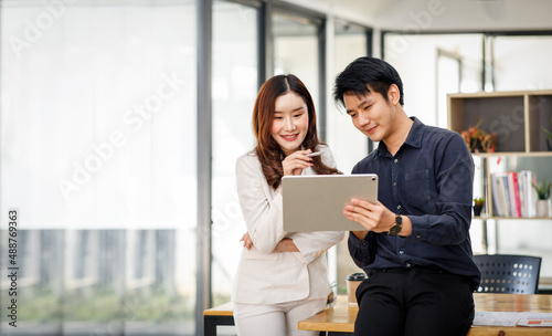 Entrepreneur Asian businessman and businesswoman discussing new business project in tablet in modern Meeting In Modern Office, Asian business casual concept.
