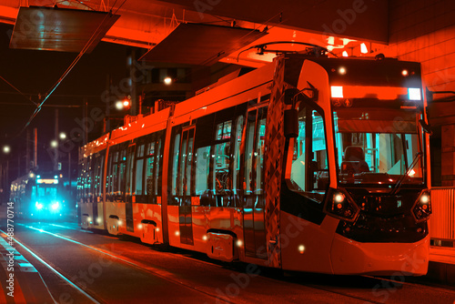 Red tram close-up at the bus stop, no people. Modern urban transport at night in the city.