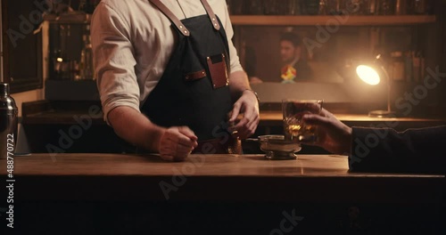 Caucasian male customer drinking alone at bar while engaging with bartender 