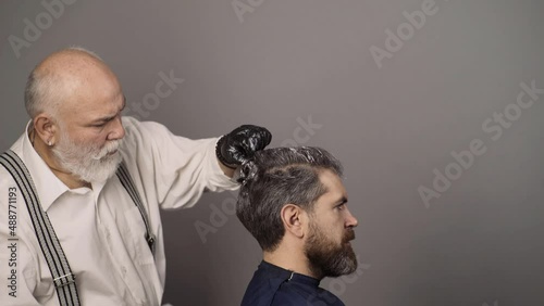 Hair salon, hair coloring man. Attractive senior barber doing a haircut and haircolor for client at barber shop. Senior hairdresser drying hair.